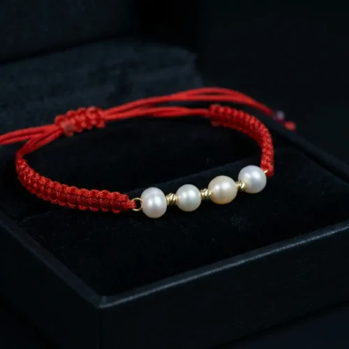 Bracelet fin en cordon rouge tressé avec quatre véritables perles Jouher et petites perles en or 18 carats, présenté dans un écrin de luxe ScooBijou.