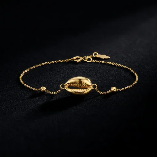 Craquez pour ce bracelet fin en Or massif 18K. Motif coquillage (Wda3) élégant, chaîne délicate et petite Khmisa porte-bonheur. Livraison au Maroc. Texte ALT image Bracelet fin en chaîne d'or massif 18 carats avec un motif central en forme de coquillage cauri, de petites perles dorées et un mini pendentif Khmisa près du fermoir, sur fond noir.