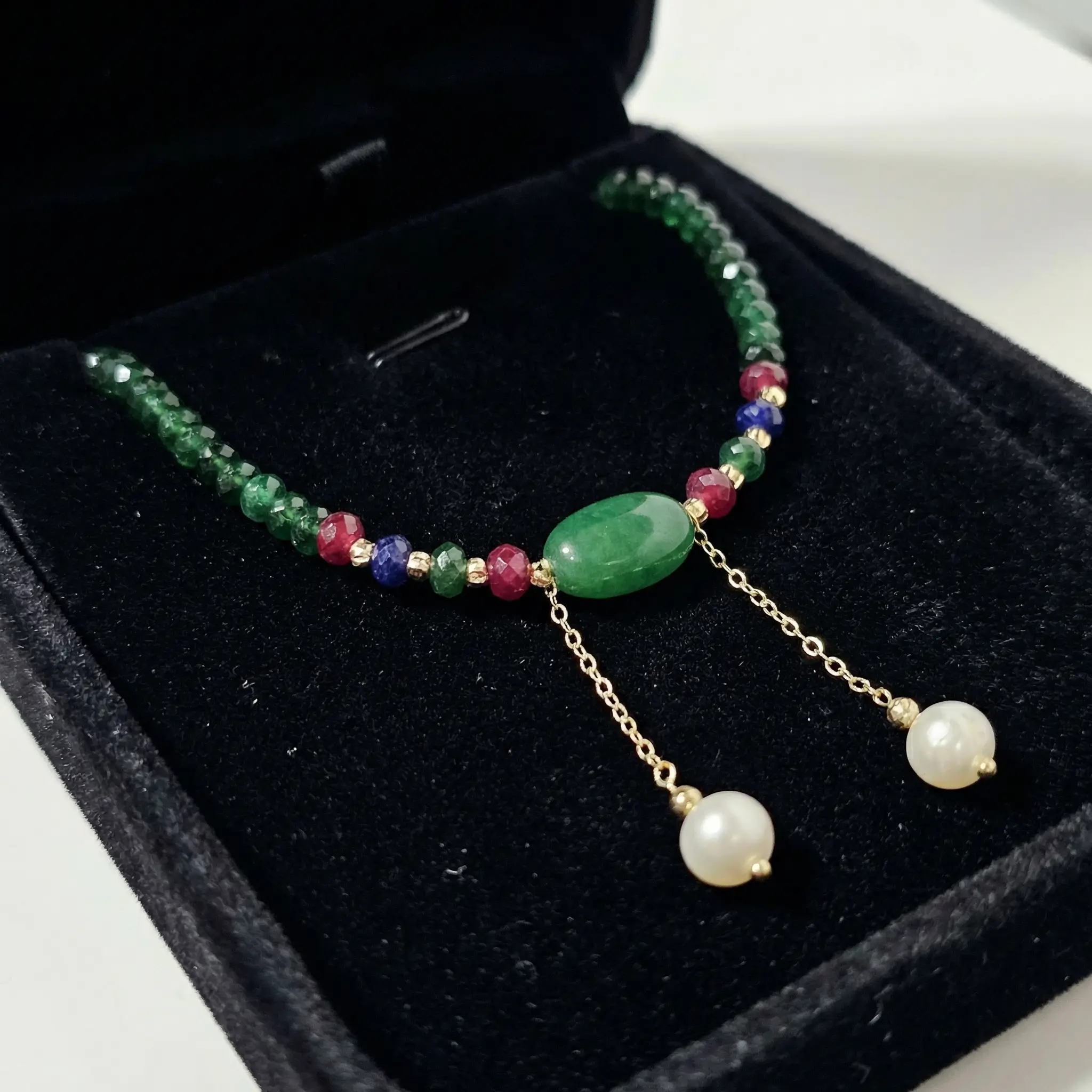 Collier élégant en perles d'émeraude synthétique vertes avec fermoir en macramé ajustable, détails en or 18 carats et deux perles de culture pendantes sur fond noir.