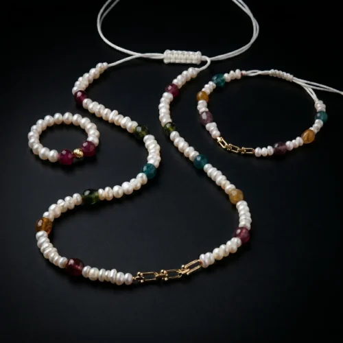 Ensemble de bijoux de luxe comprenant un collier, un bracelet ajustable et une bague assortie en perles d'eau douce, pierres de tourmaline et détails en or 18 carats sur fond noir.