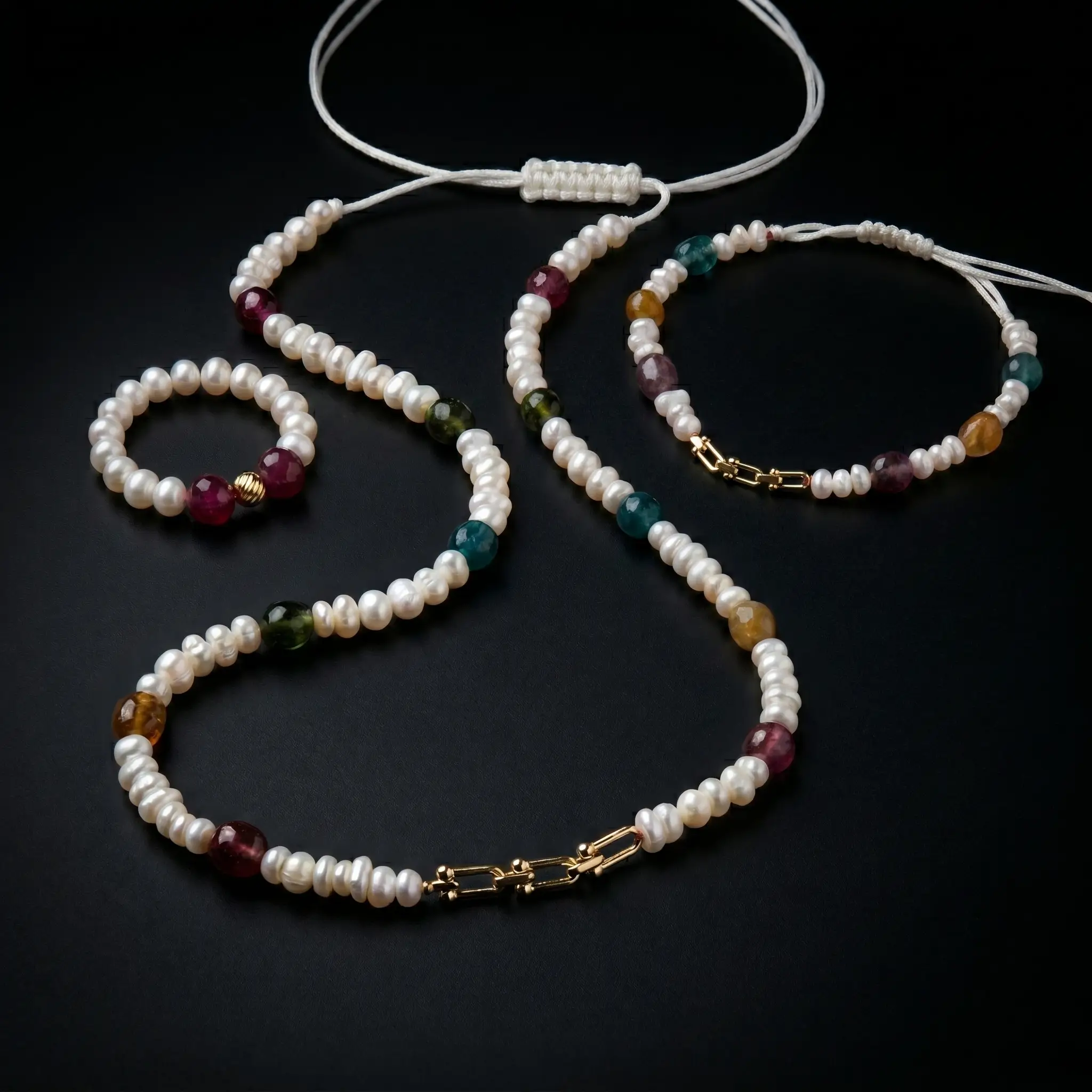 Ensemble de bijoux de luxe comprenant un collier, un bracelet ajustable et une bague assortie en perles d'eau douce, pierres de tourmaline et détails en or 18 carats sur fond noir.