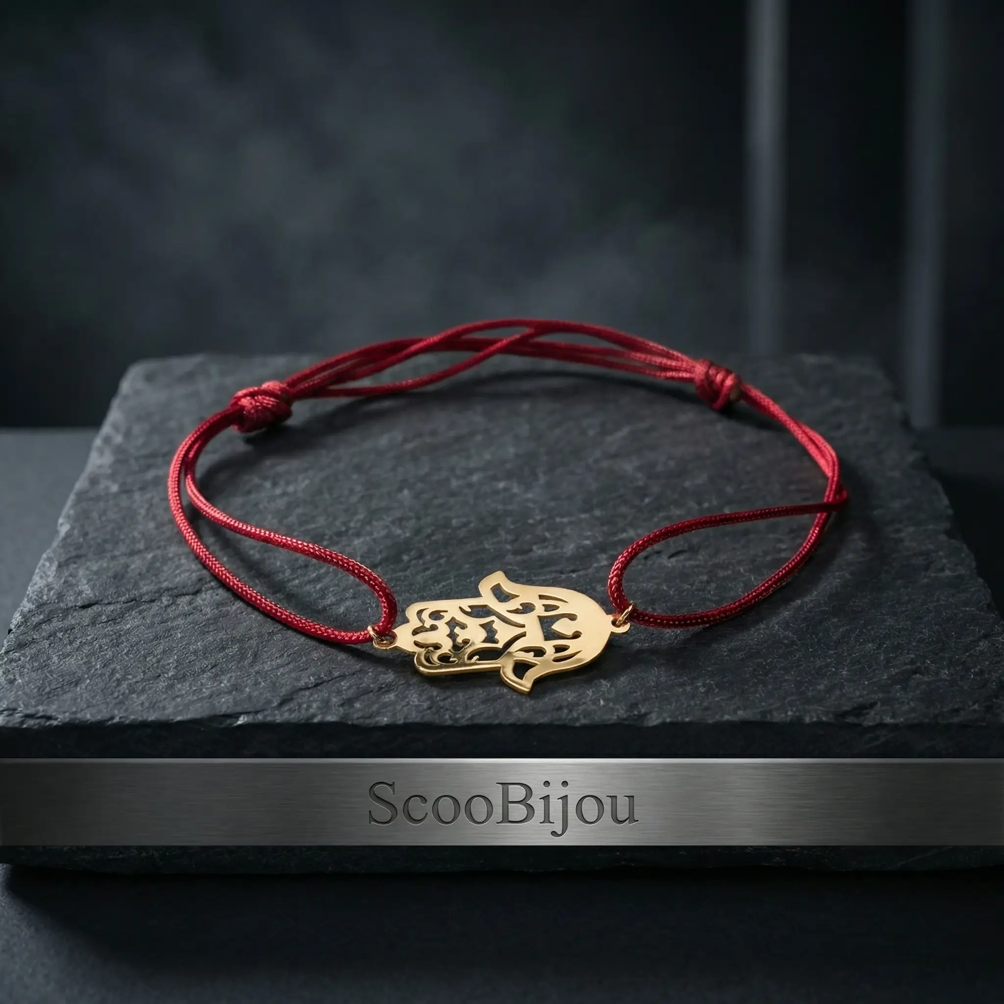Bracelet porte-bonheur en cordon rouge ajustable avec un pendentif central en forme de Khamsa (Main de Fatma) finement découpé en Or 18 carats sur un fond noir luxueux.