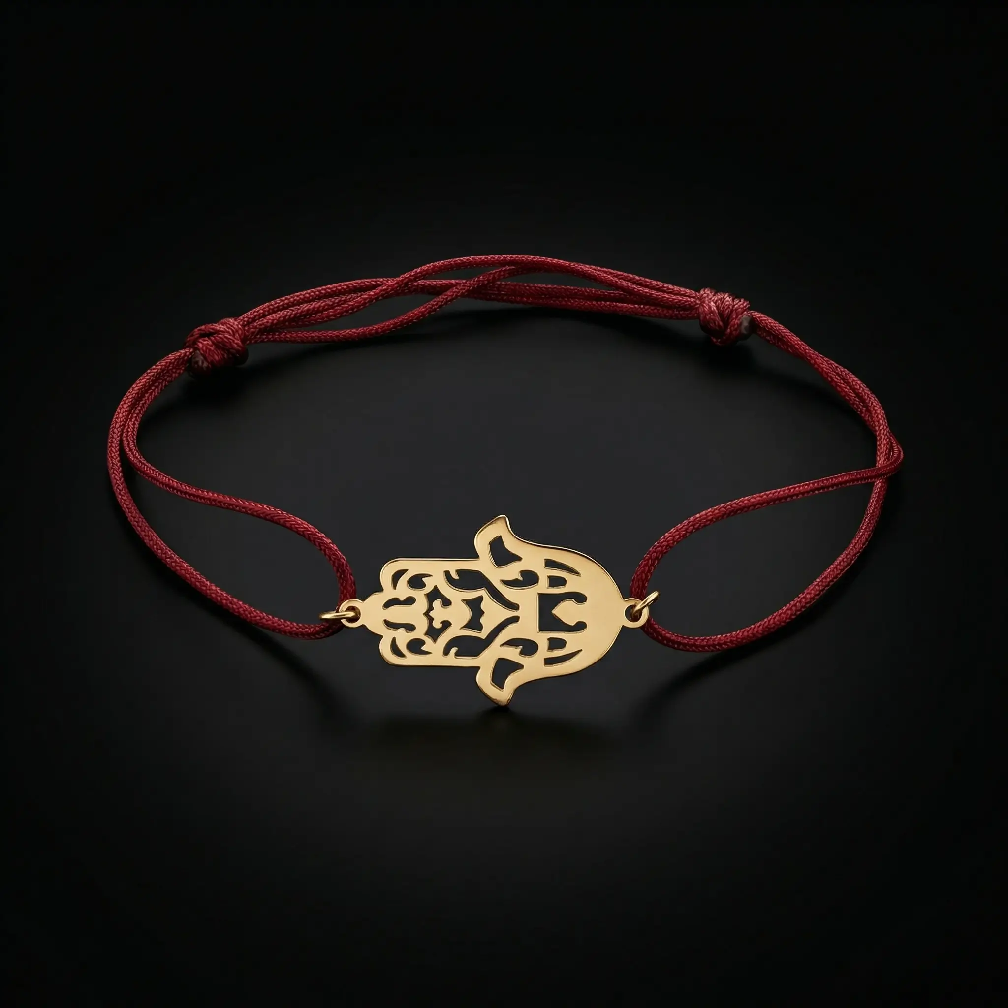 Bracelet porte-bonheur en cordon rouge ajustable avec un pendentif central en forme de Khamsa (Main de Fatma) finement découpé en Or 18 carats sur un fond noir luxueux.