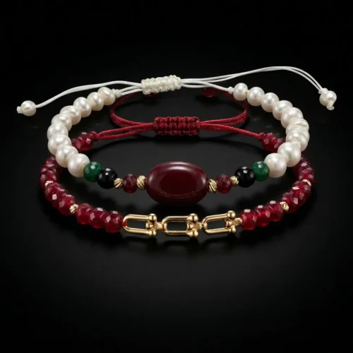 Duo de bracelets ajustables en macramé avec véritables perles d'eau douce, émeraude synthétique, pierres rouges et finitions en or 18K dans un écrin noir.