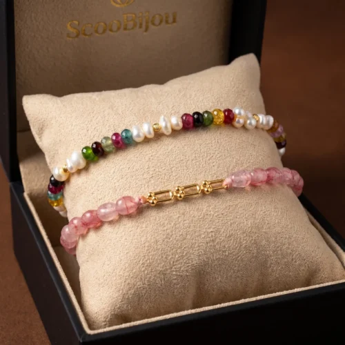 Duo de bracelets ajustables en macramé présentés dans un écrin noir, ornés de véritables perles d'eau douce, de tourmalines multicolores et roses, et de maillons en or 18K.