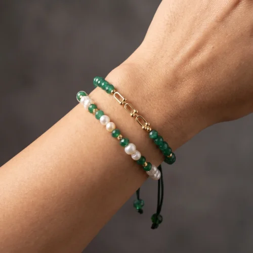 Duo de bracelets ajustables en macramé vert foncé ornés de véritables perles d'eau douce, de pierres vertes facettées et de finitions géométriques en or 18K, présentés dans un écrin noir.