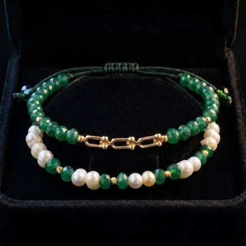 Duo de bracelets ajustables en macramé vert foncé ornés de véritables perles d'eau douce, de pierres vertes facettées et de finitions géométriques en or 18K, présentés dans un écrin noir.